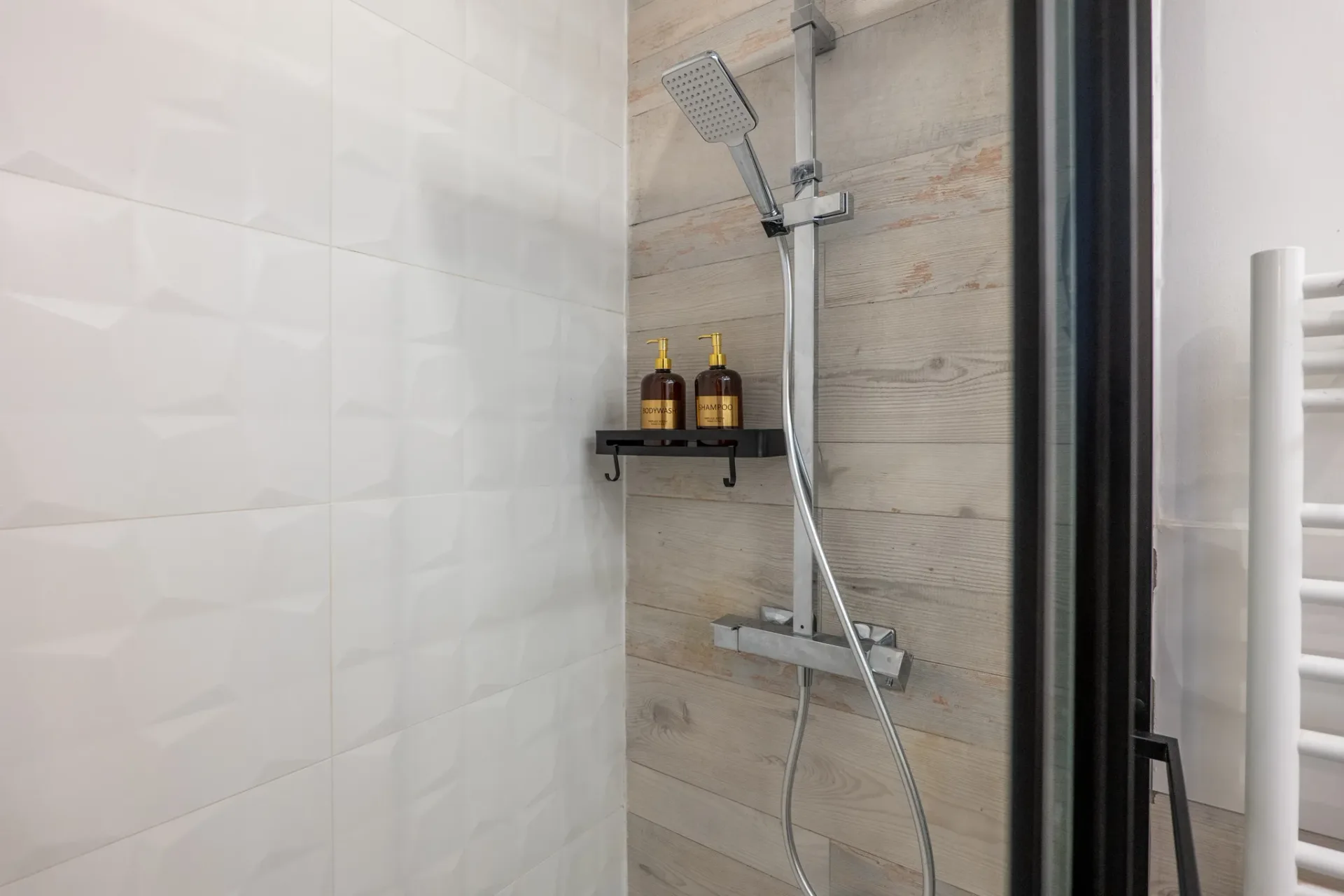 Détail de la douche à l'italienne avec bois patiné et produits d'accueil dans l'appartement à Manosque.