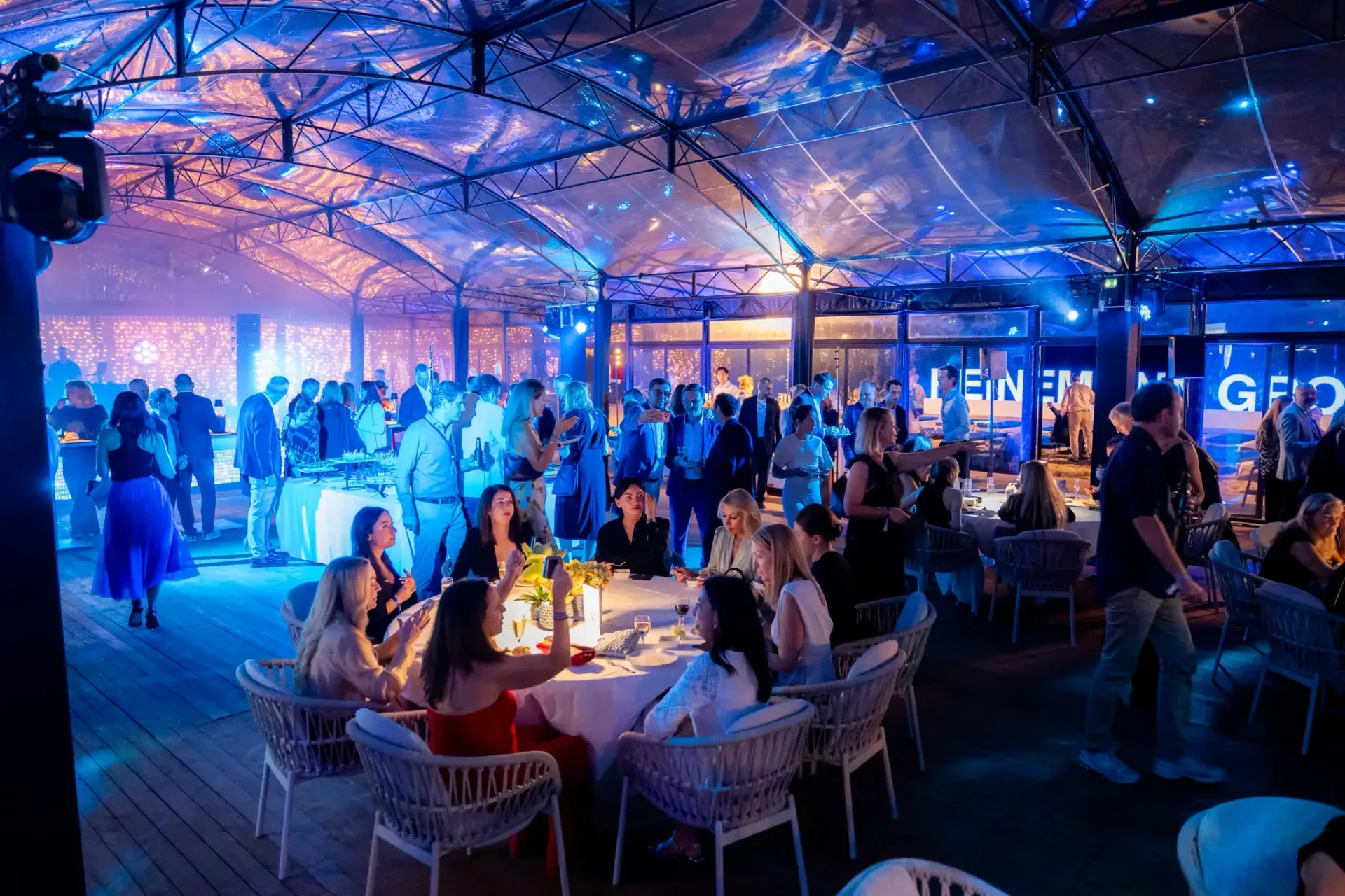 Dinner under the blue-lit glass roof of Palais Stéphanie Beach in Cannes, guest tables at the Gebr. Heinemann gala evening, event photographer.