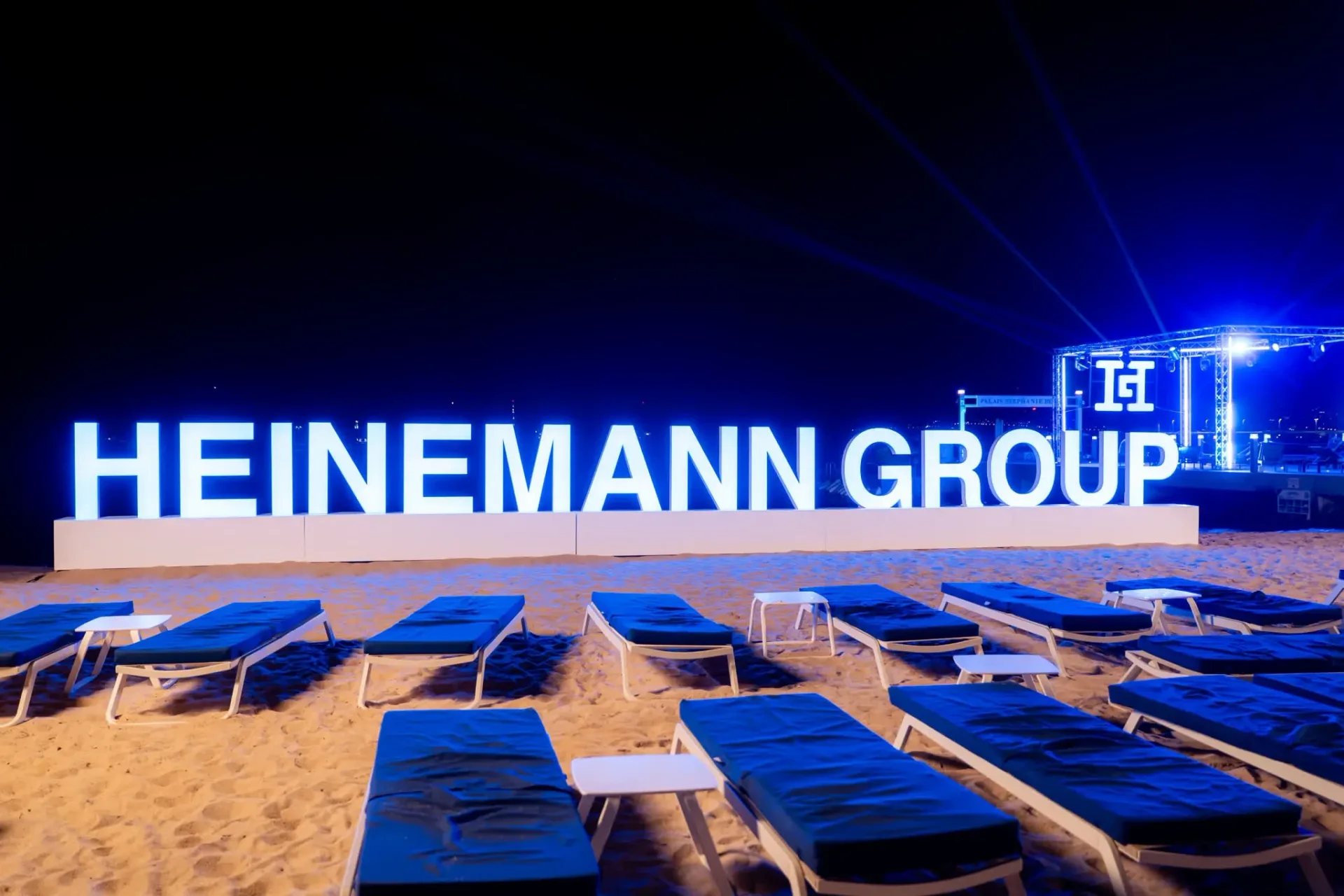 Illuminated Heinemann Group letters on the Cannes beach with blue sun loungers in the foreground, set design of the annual gala evening, event photographer.