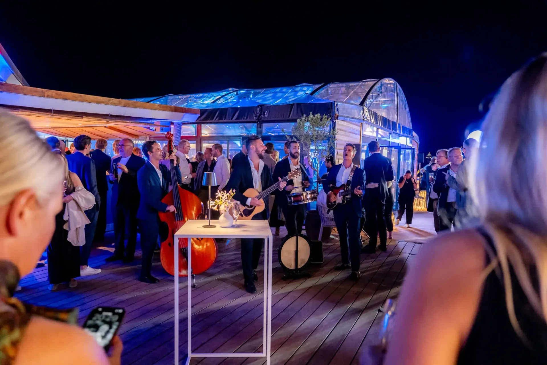 Live musicians playing on the deck of Palais Stéphanie Beach during the Heinemann gala evening in Cannes, guests in evening wear, event photo report.