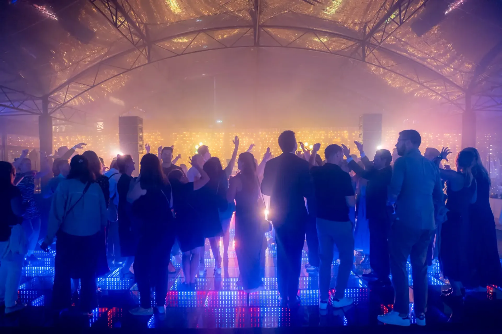 Invités les bras levés sur la piste de danse lumineuse, fin de soirée de gala Heinemann à Cannes, reportage photo événementiel de nuit.