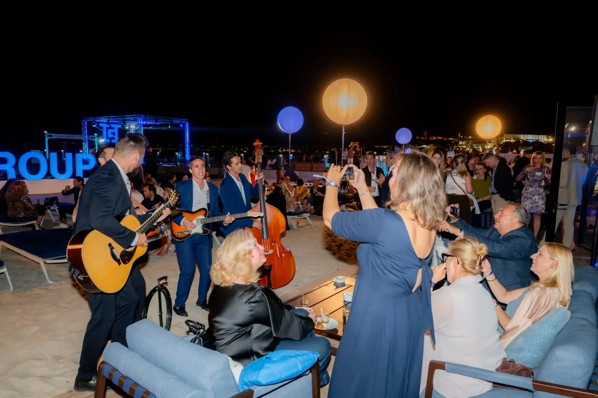 Une invitée photographie les musiciens avec son téléphone sur la plage, ambiance conviviale de la soirée de gala Heinemann à Cannes, reportage photo d'événement d'entreprise.