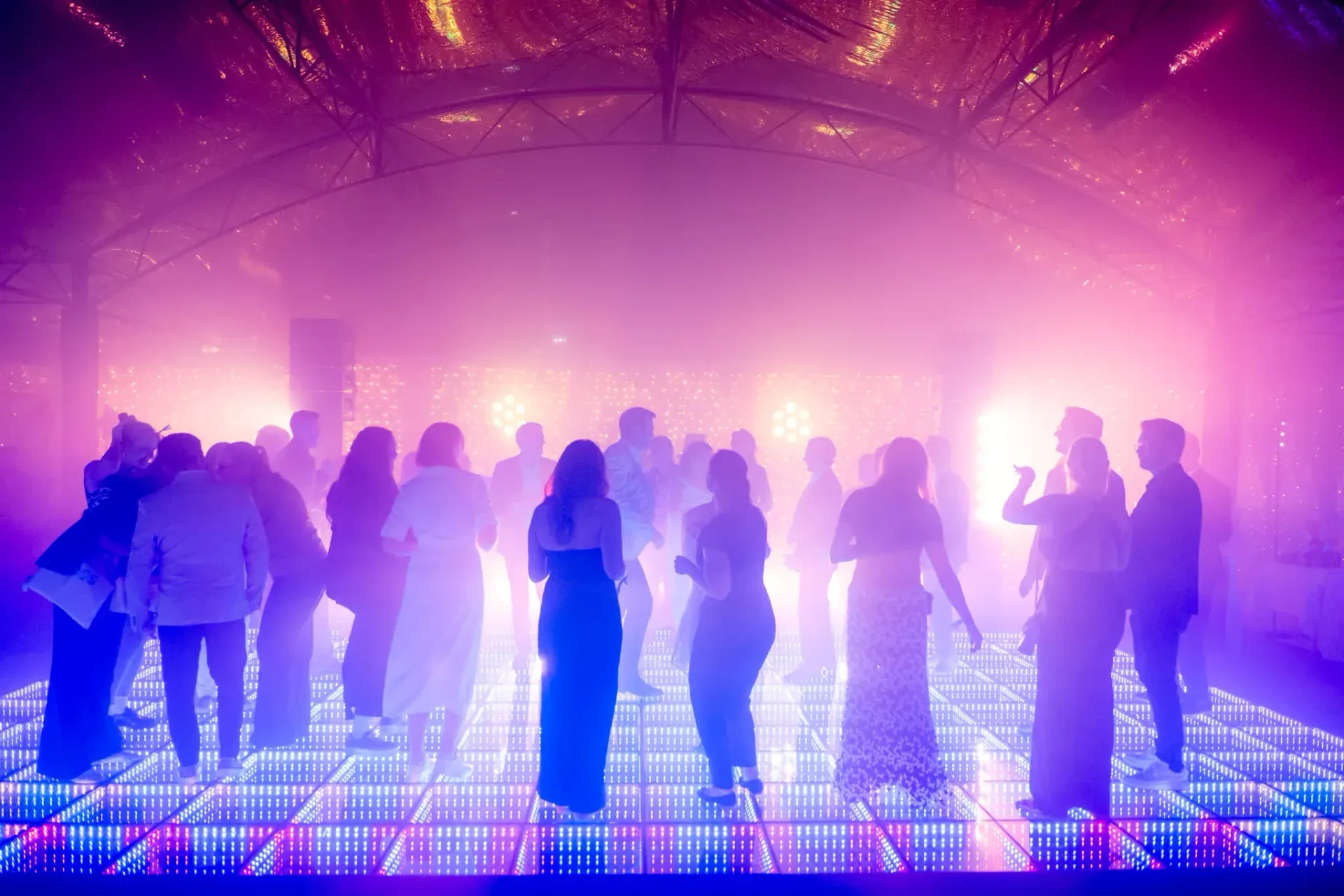 Piste de danse LED sous la verrière dans une ambiance violette et rose, invités dansant lors de la soirée Connect & Celebrate de Gebr. Heinemann à Cannes.