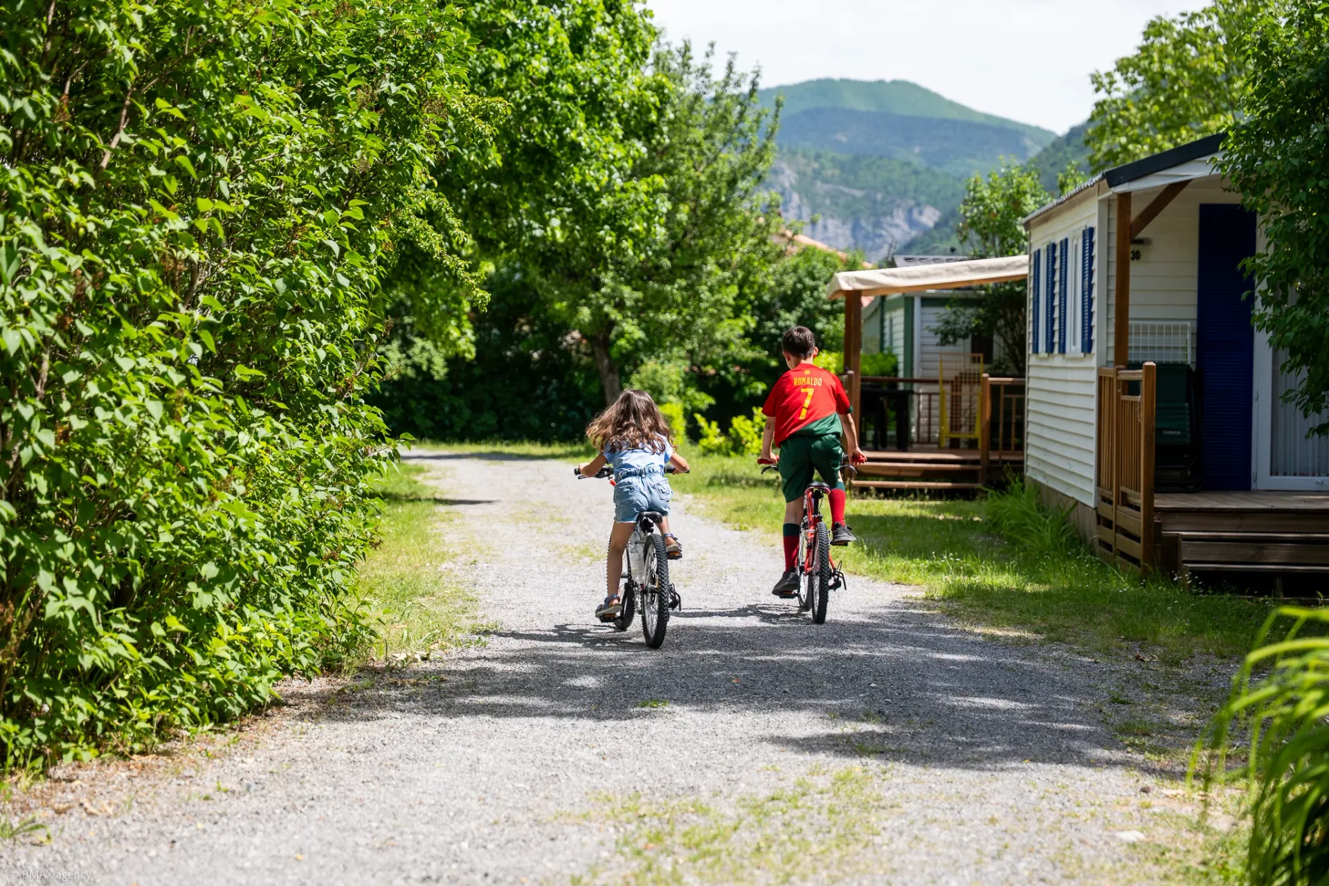 Enfants à vélo dans une allée ombragée du camping La Ribière