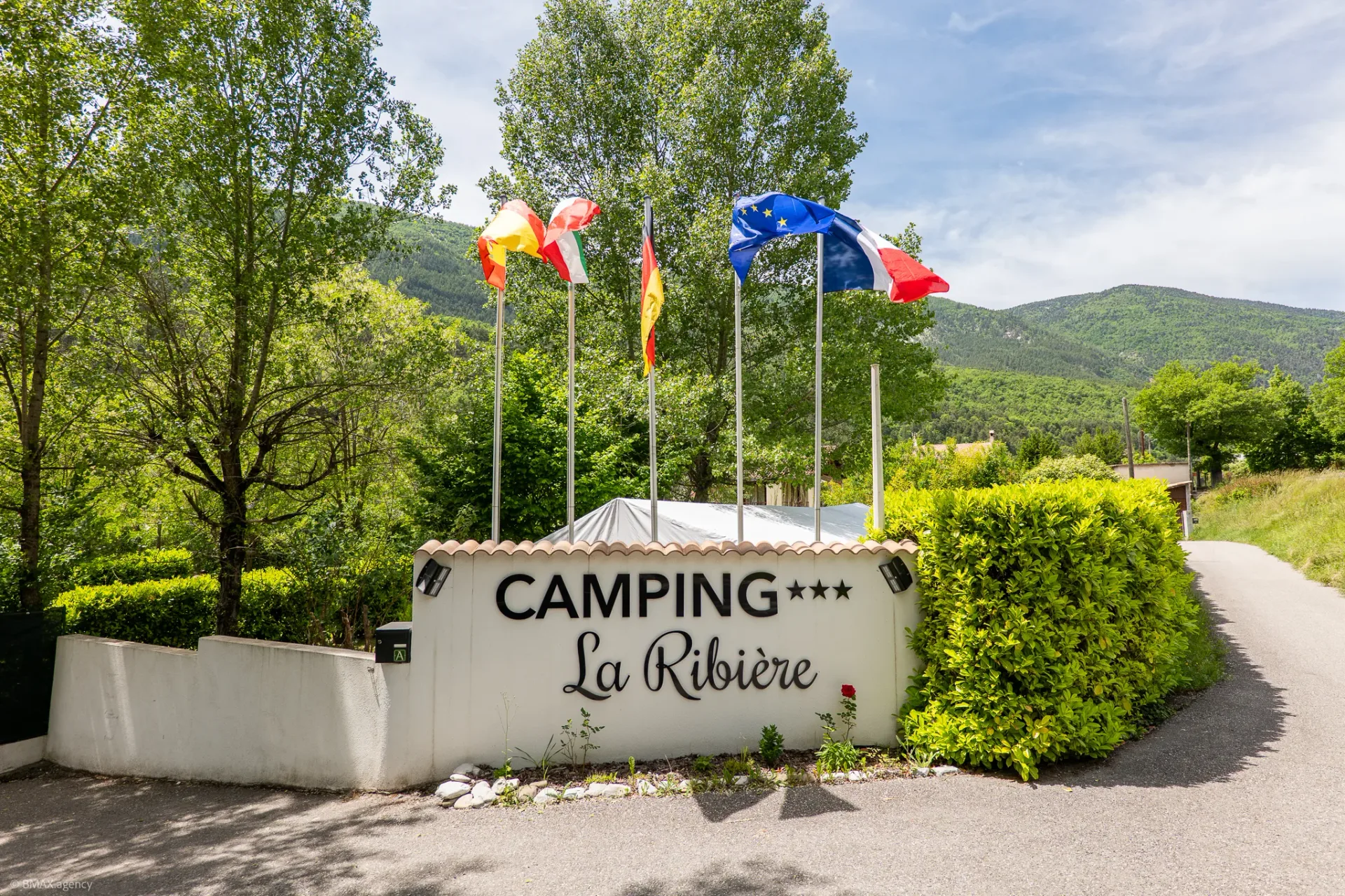 Entrée du camping La Ribière à Annot avec panneau d'accueil et drapeaux