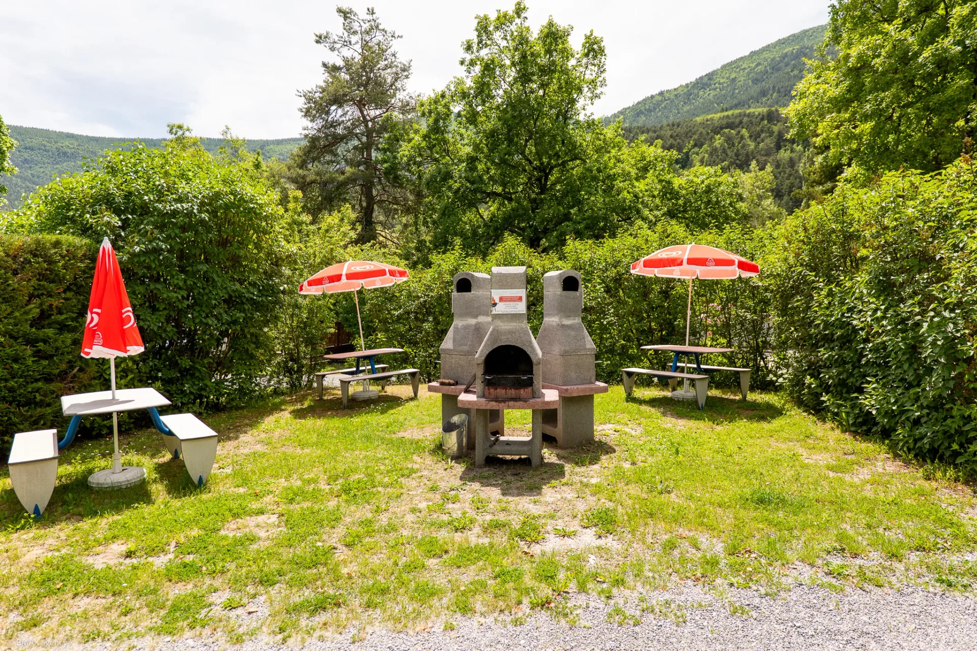 Espace pique-nique avec tables, parasols et barbecues collectifs, camping La Ribière